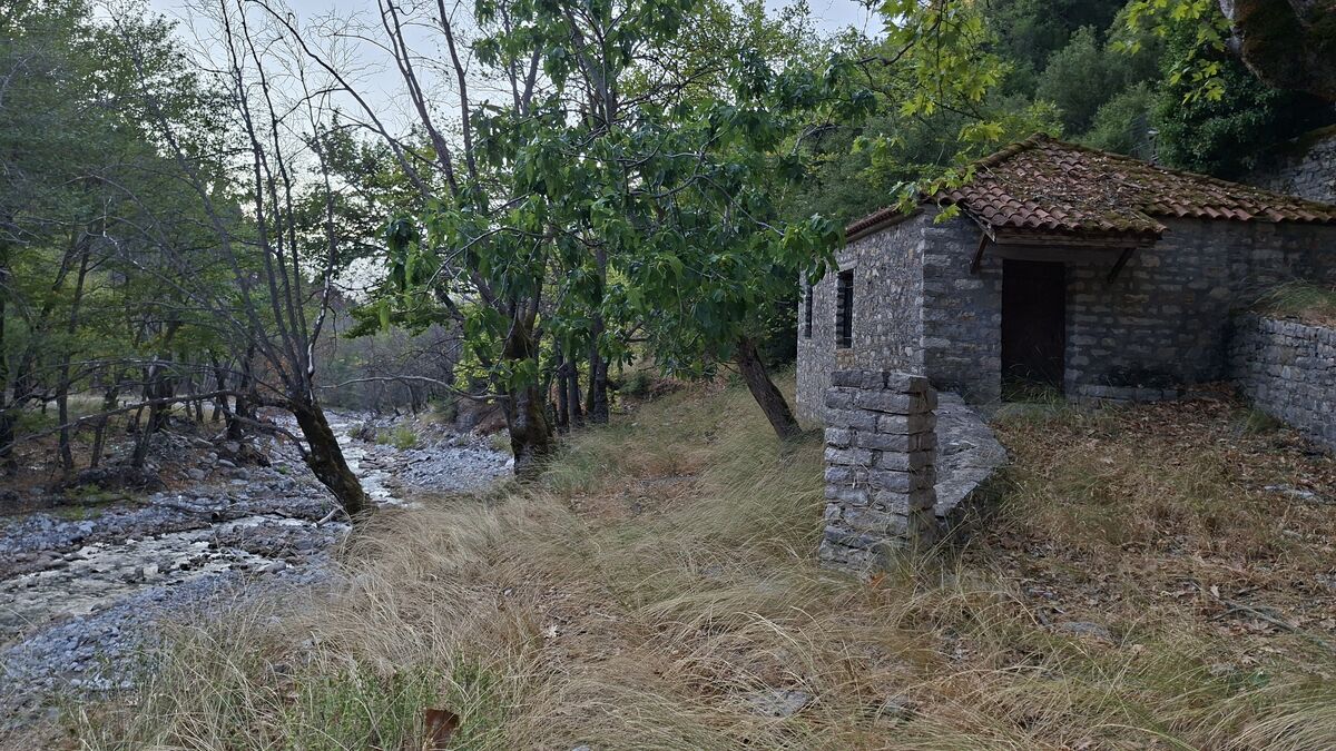 Ο πέτρινος νερόμυλος με την κεραμοσκεπή, δίπλα στην κοίτη του ρέματος, ανάμεσα σε καρυδιές και πλατάνια