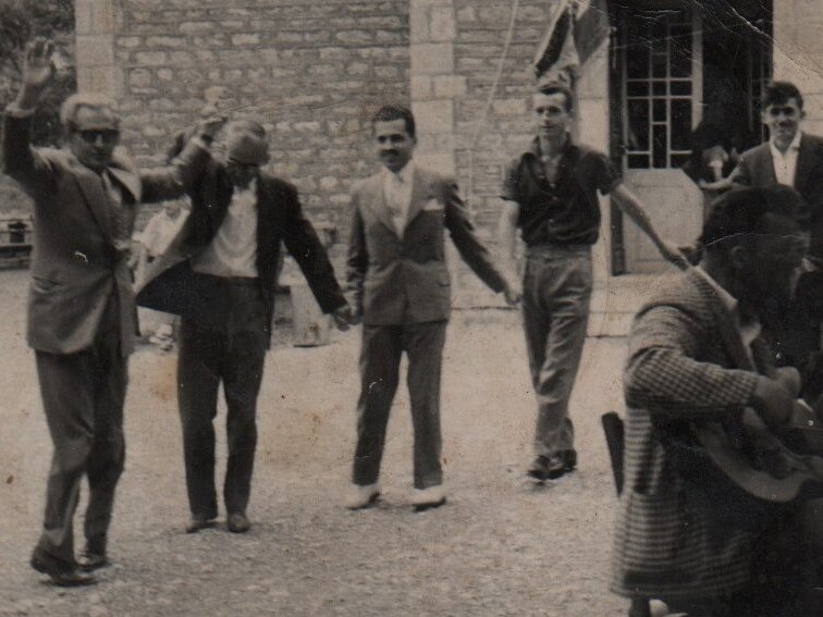 Παλιά φωτογραφία από το πανηγύρι — άνδρες χορεύουν στον προαύλιο χώρο της εκκλησίας, με λαουτιέρη δεξιά