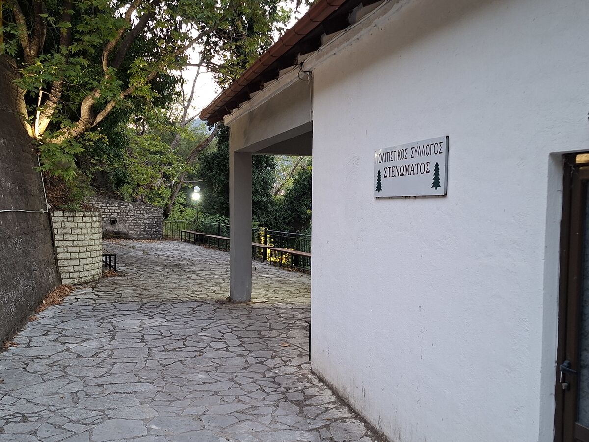 Το κτίριο του συλλόγου στην Πέρα Βρύση, με την πινακίδα «Πολιτιστικός Σύλλογος Στενώματος» και το πλακόστρωτο κάτω από τα πλατάνια